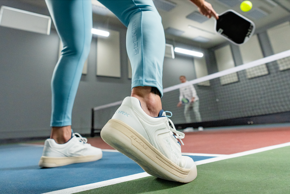 A close-up image shows a woman pivoting her feet in the Selkirk Legacy pickleball shoes. 