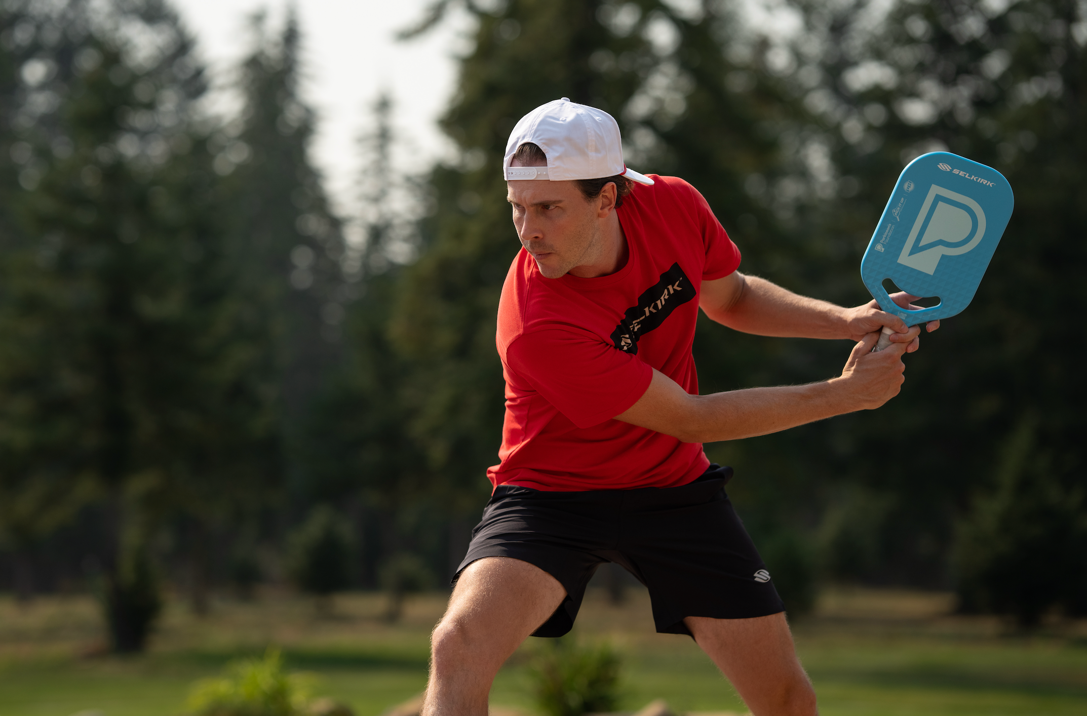 A man prepares to hit a backhand drive using a Selkirk x Parkinson's paddle. 
