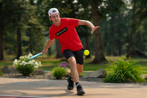 A man prepares to serve a pickleball during an outdoor singles game. 