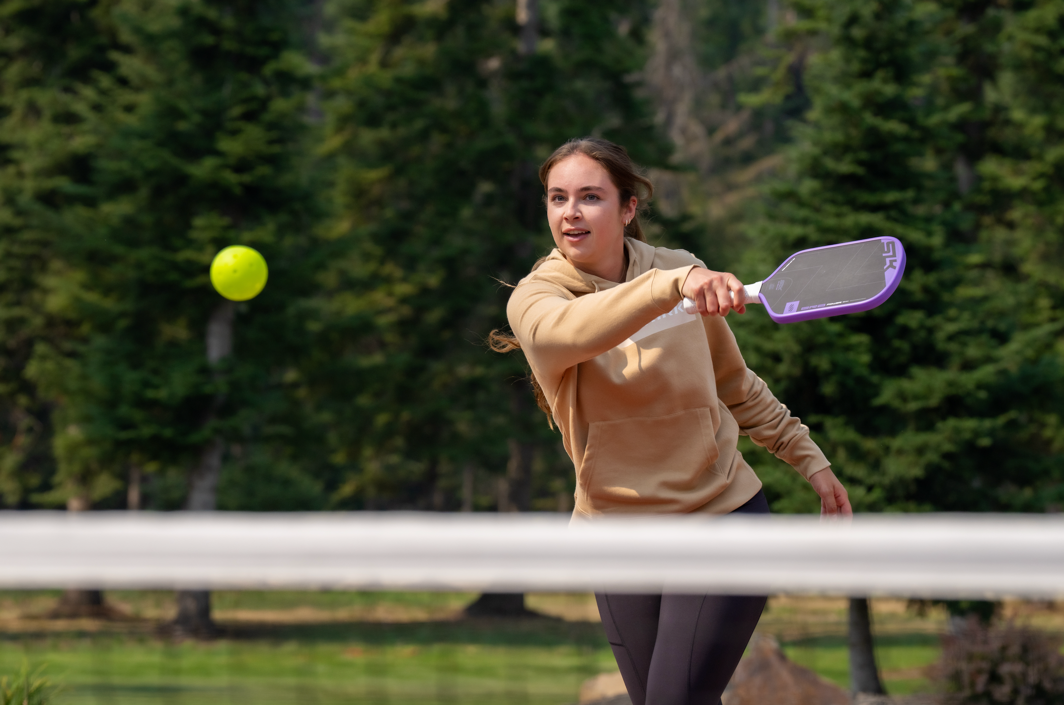 A woman wears several Selkirk layers as she plays outdoor pickleball in the fall. 