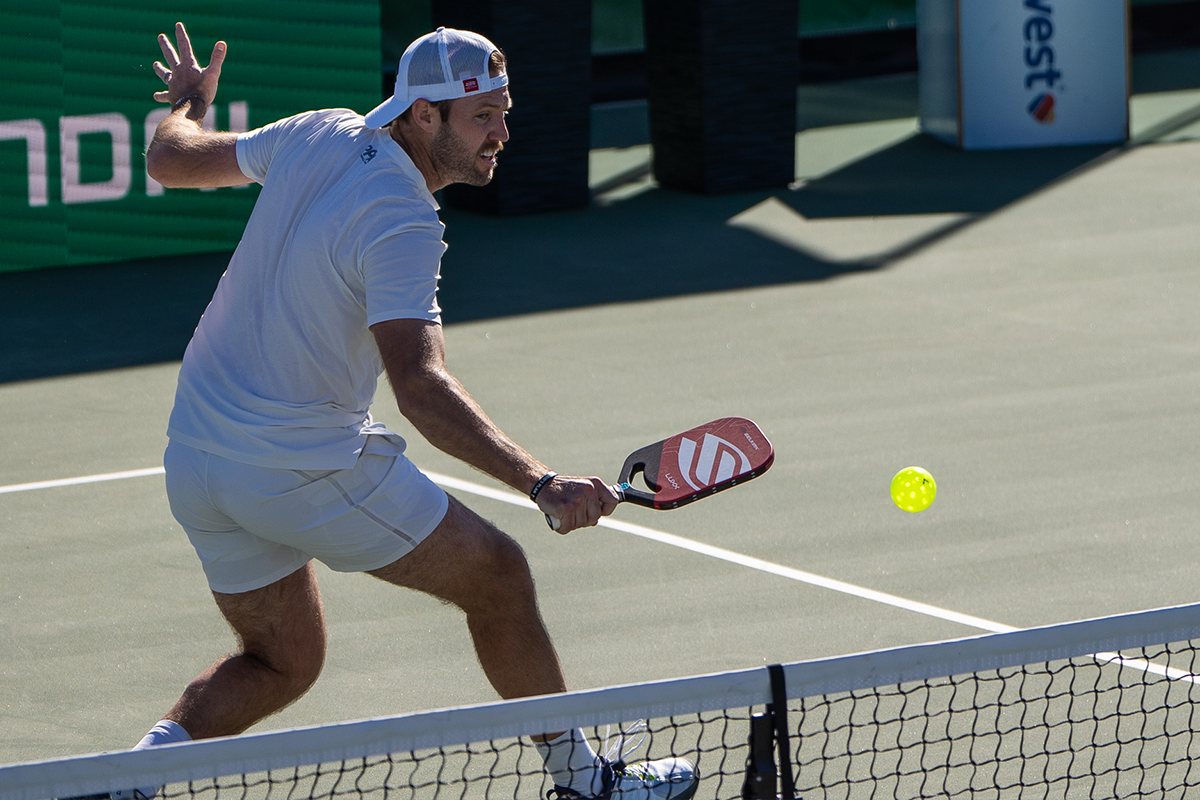 A player in white hitting a pickleball during a match.