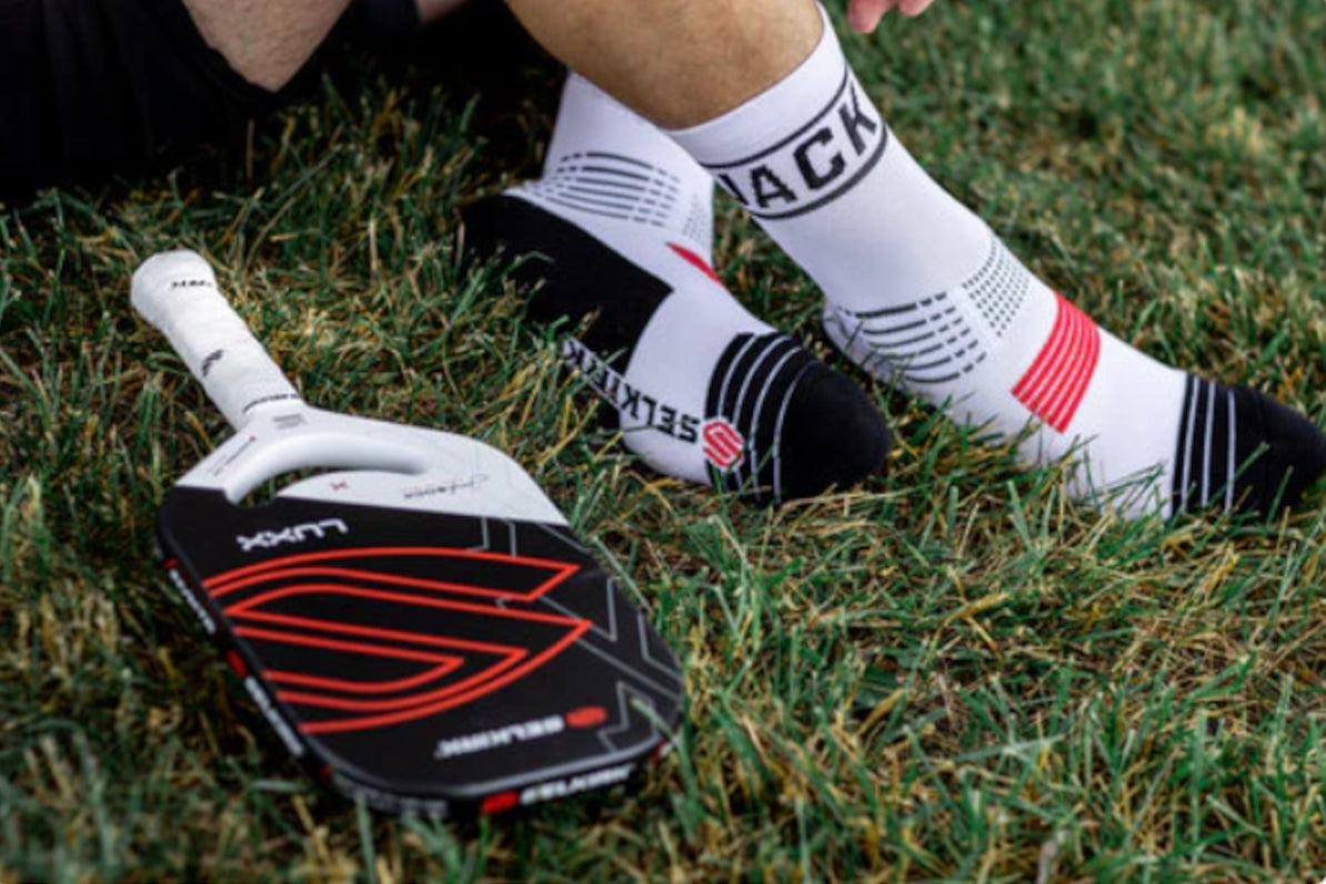 A person sitting on grass wearing pickleball socks and holding a pickleball paddle.