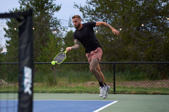 A man is in mid-run as he hits a pickleball on an outdoor court. 