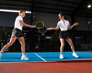 Two women smile as they tap pickleball paddles after winning a point. 