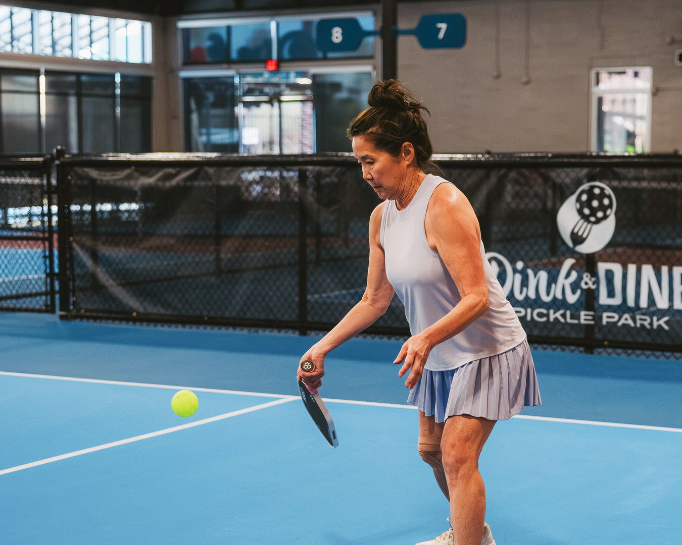 A woman performs a third shot drop from the transition zone of a pickleball court. 