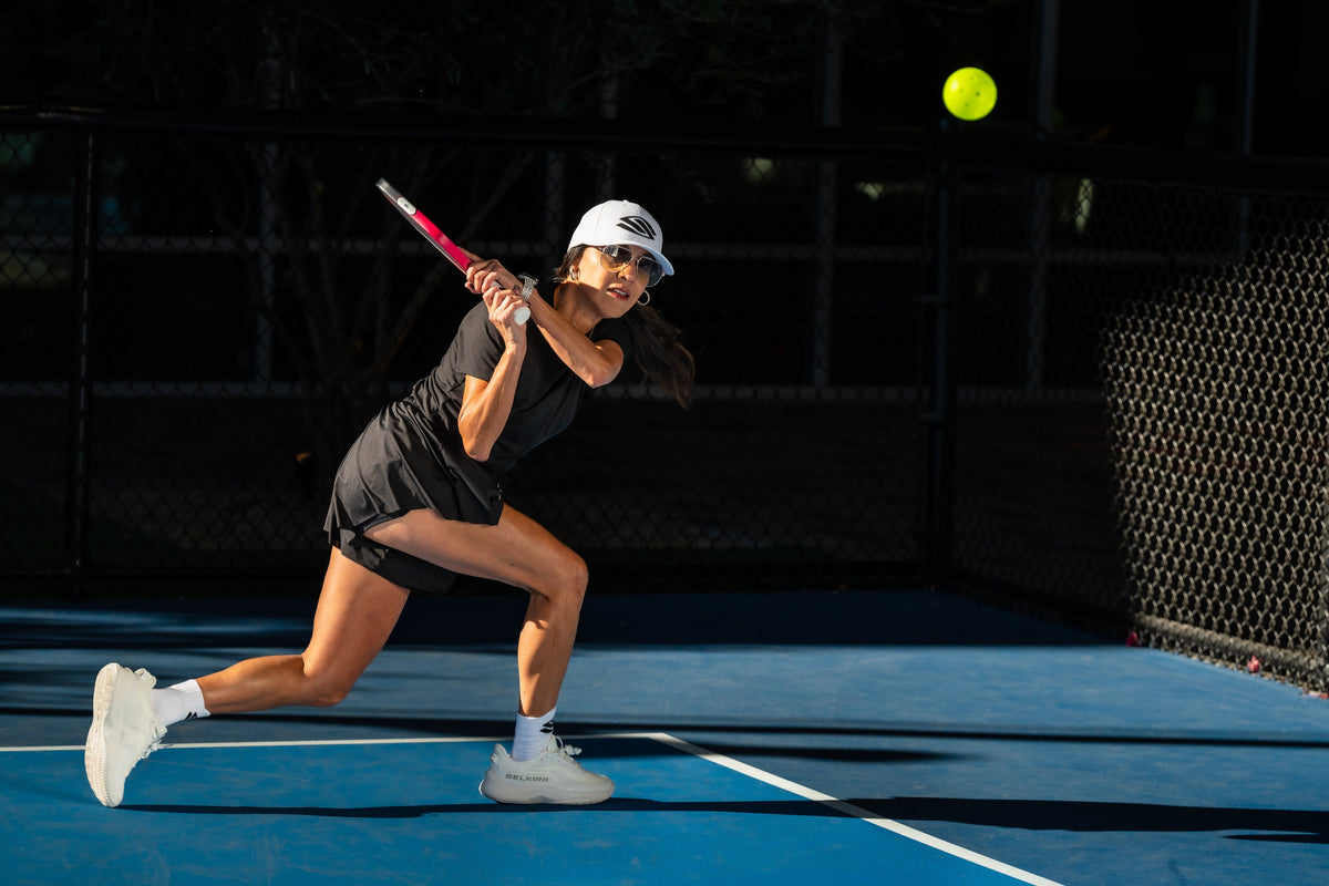 A woman hits a backhand drive on an outdoor pickleball court. 