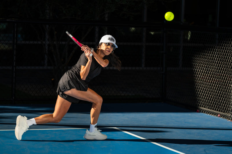 A woman hits a backhand drive on an outdoor pickleball court. 