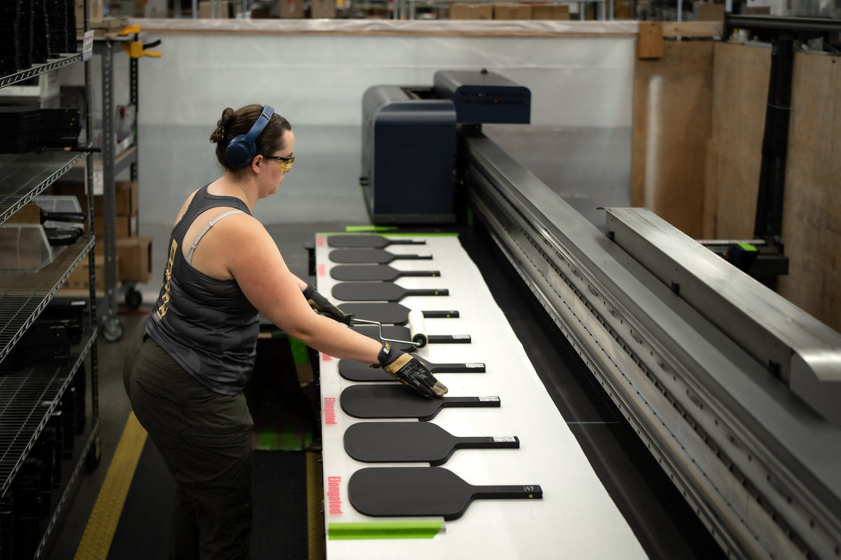 A woman aligns different pickleball paddle faces in a manufacturing warehouse. 