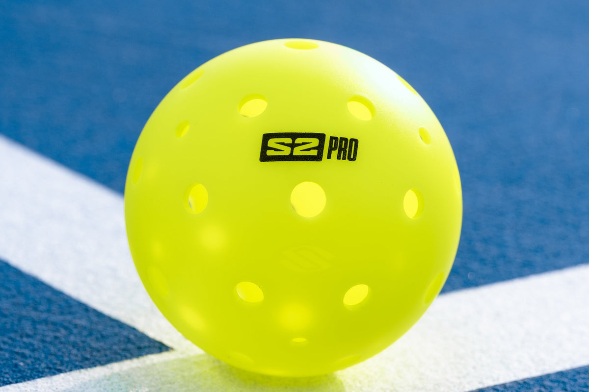 An S2 Pro pickleball sits on the baseline of an outdoor pickleball court. 