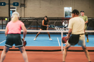 Four players play mixed doubles pickleball on an indoor pickleball court. 