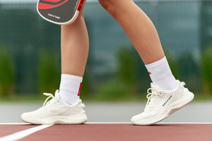 A close-up shows a person wearing Selkirk Courtlock pickleball socks with pickleball shoes. 