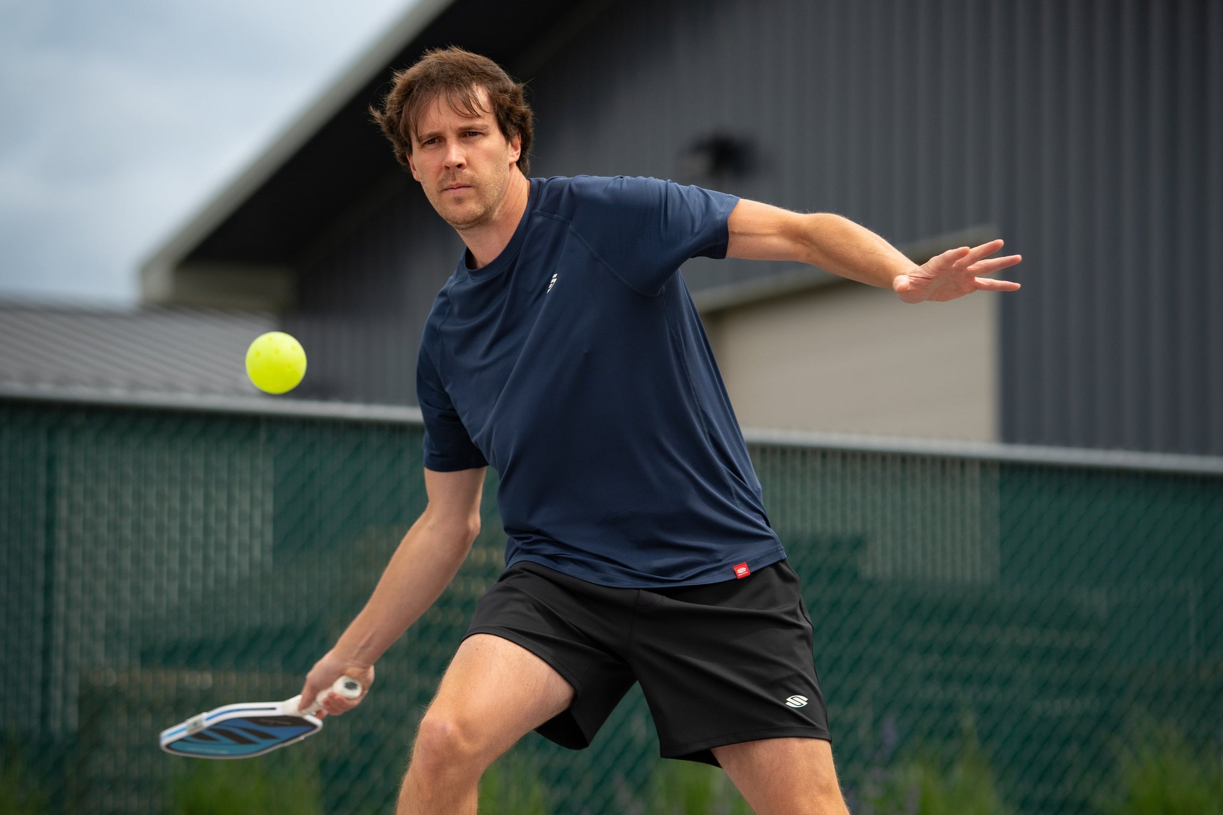 A man drops a pickleball as he prepares to serve. 
