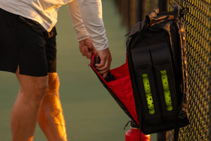A man reaches into a Selkirk Pro 2.0 pickleball bag that is hanging on a fence. 