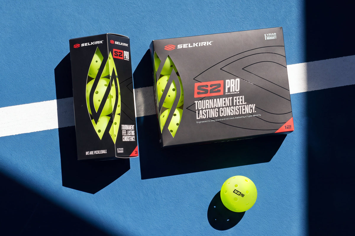 Packaged and unpackaged Selkirk S2 Pro pickleballs lay on a pickleball court. 