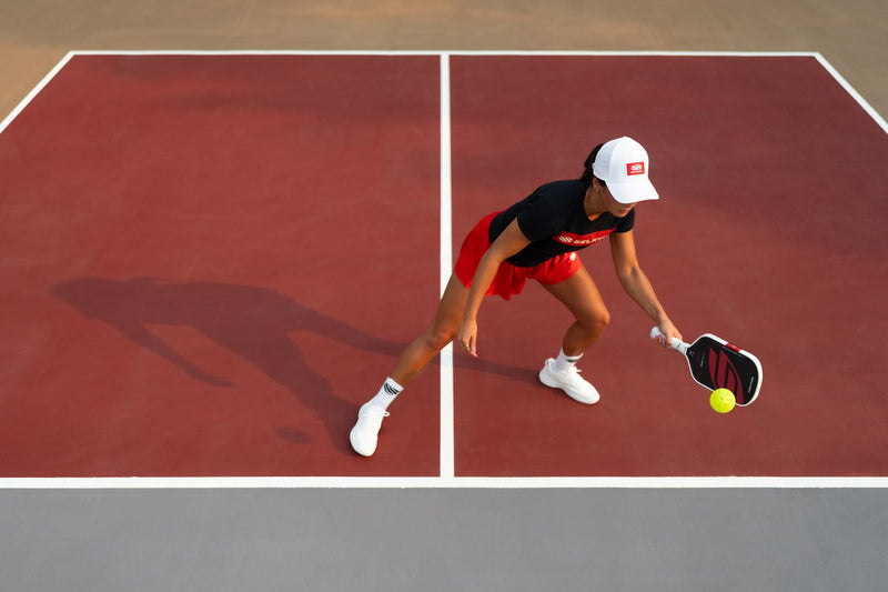 A woman bends to reach a dink with her Selkirk Boomstik on an outdoor pickleball court. 