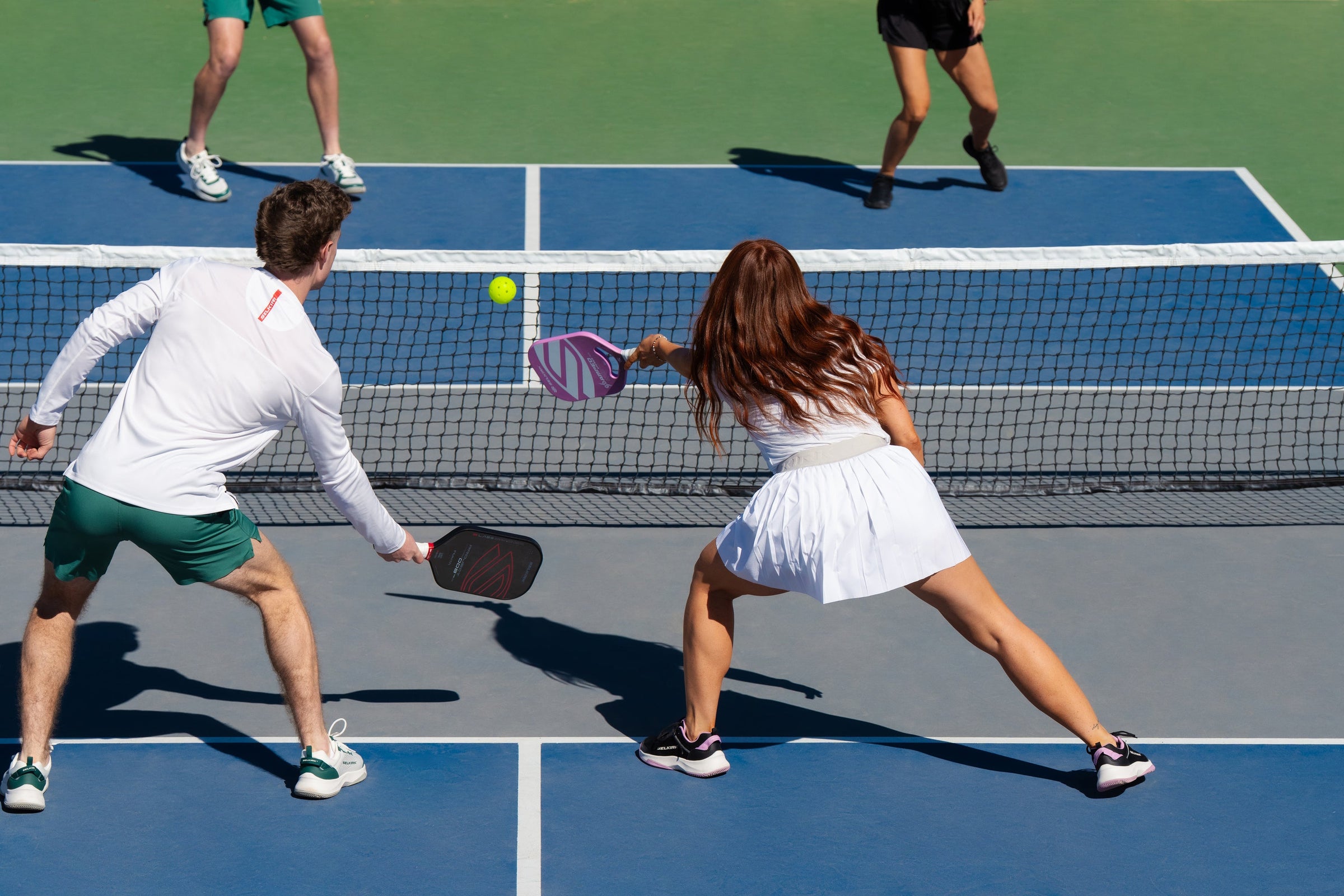 An image shows the back of a man and woman as they compete in a mixed doubles pickleball event. 
