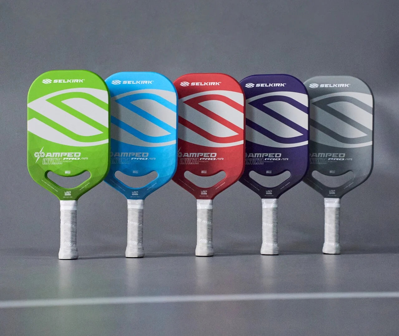 Five Selkirk AMPED Pro Air pickleball paddles in blue, red, green, purple, and gray.