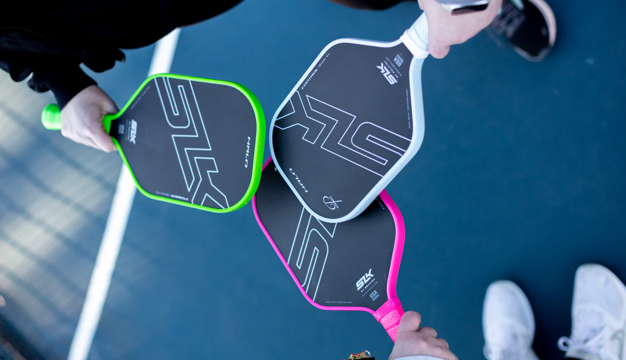 Three pickleball paddles in pink, white, and green on a court surface