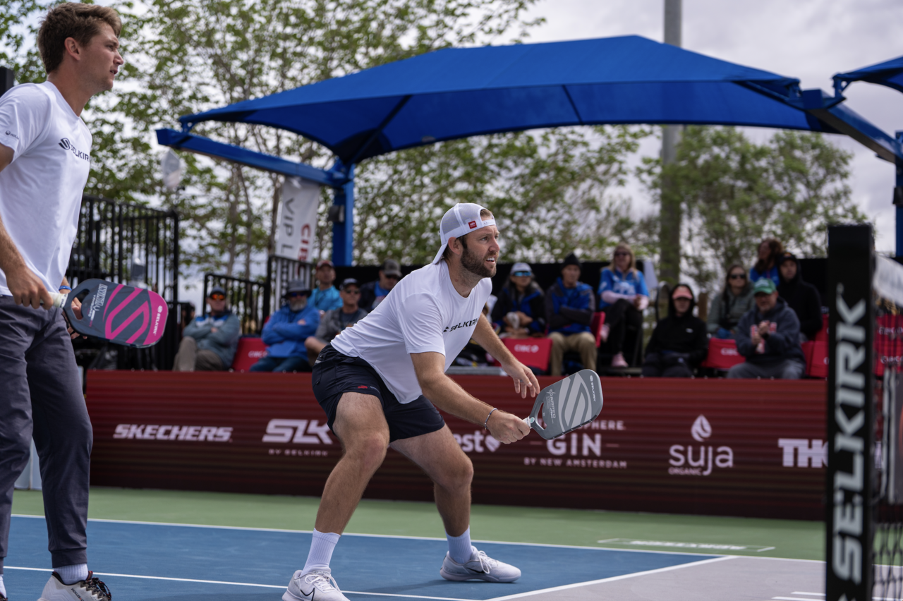 Two pickleball players preparing for a game, one in a ready position with a paddle.