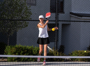 A woman serves a pickleball on an outdoor pickleball court. 