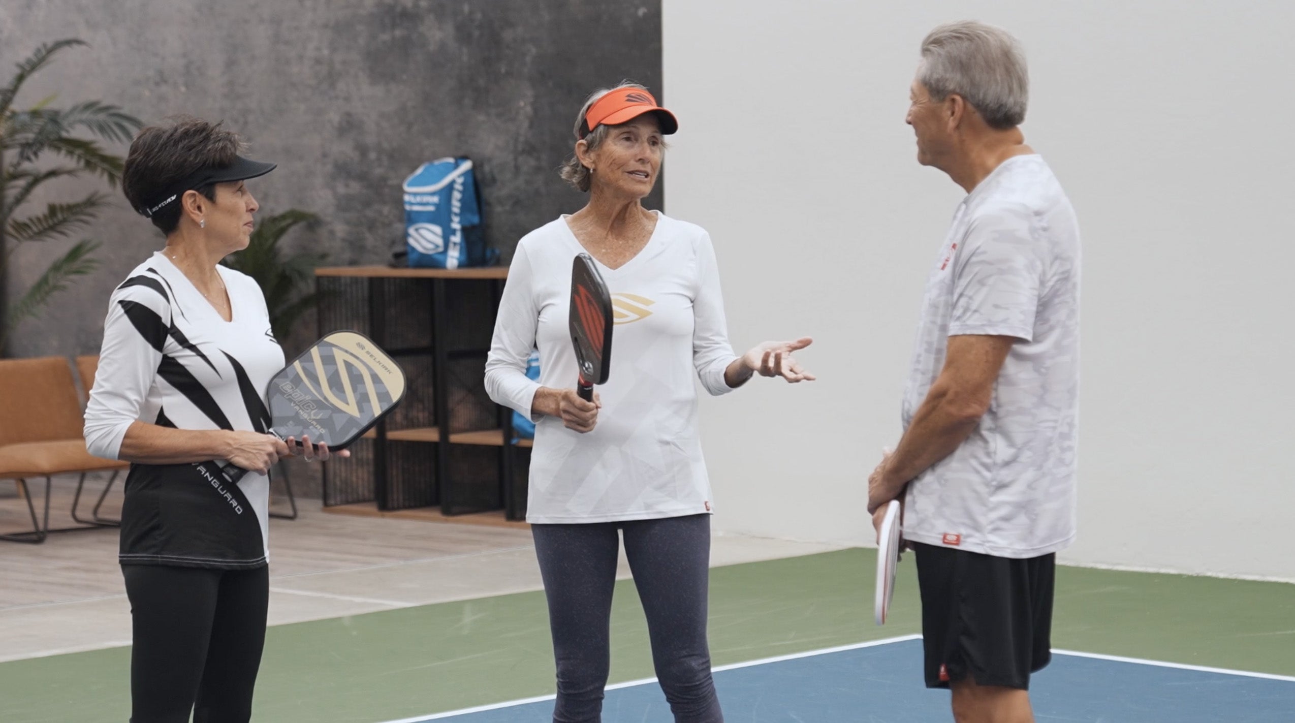 Three seniors discussing pickleball strategies on a court, holding paddles.