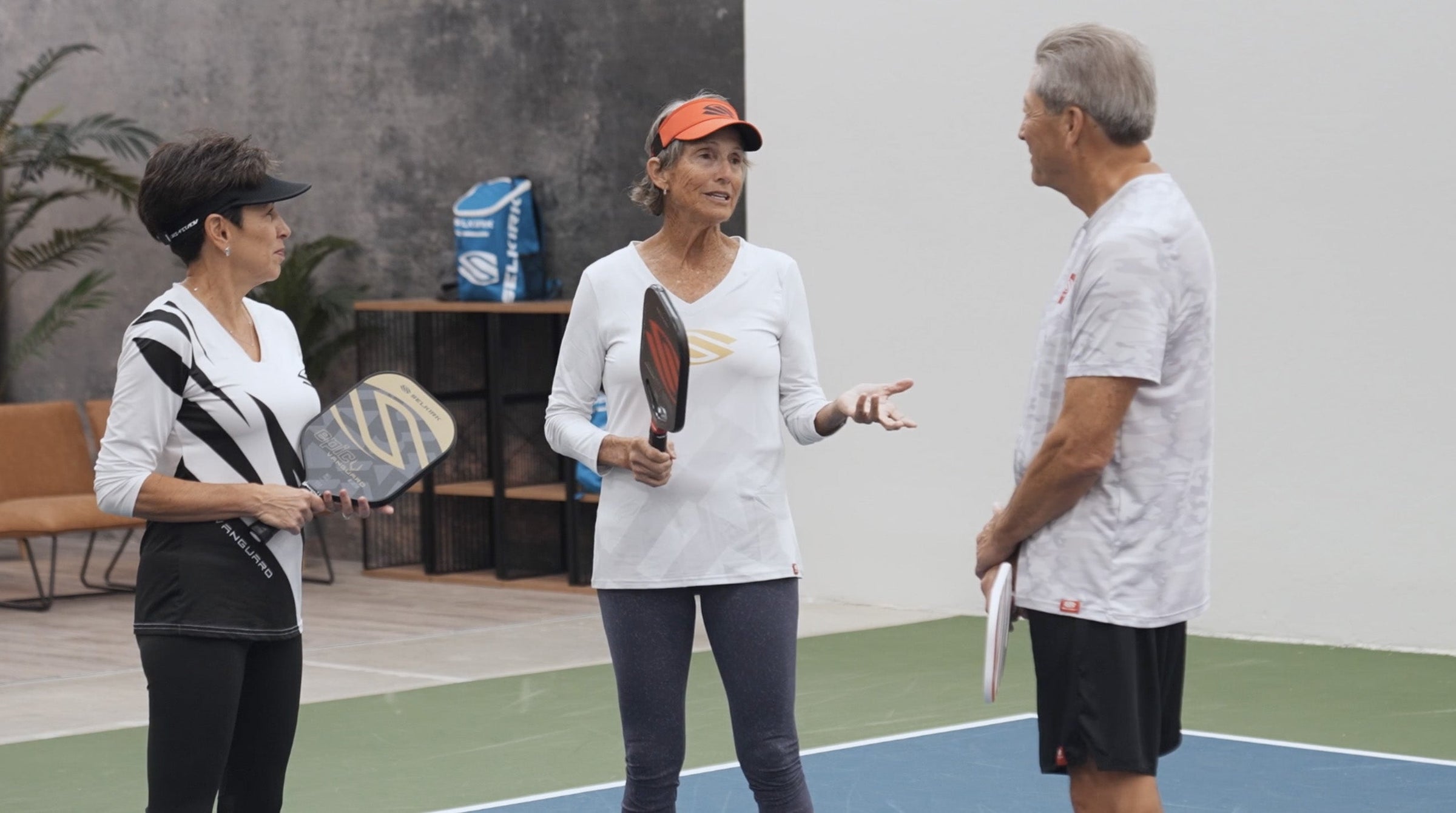 Three seniors discussing pickleball strategies on a court, holding paddles.