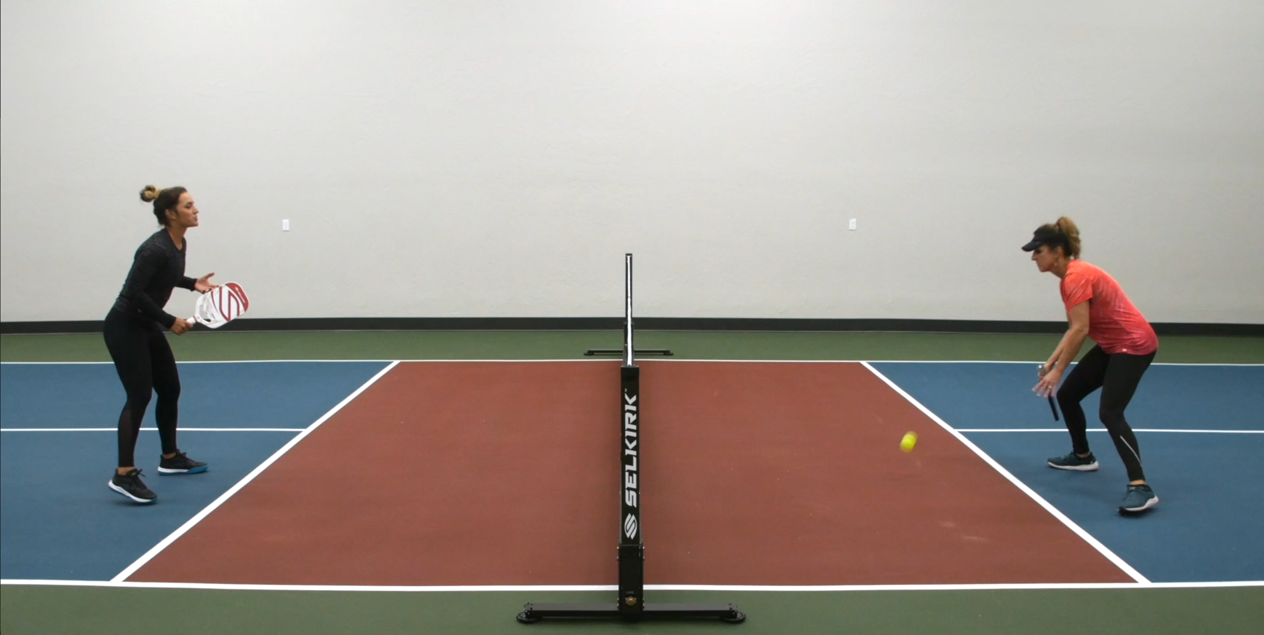Two players practicing pickleball warm-up drills on a court.