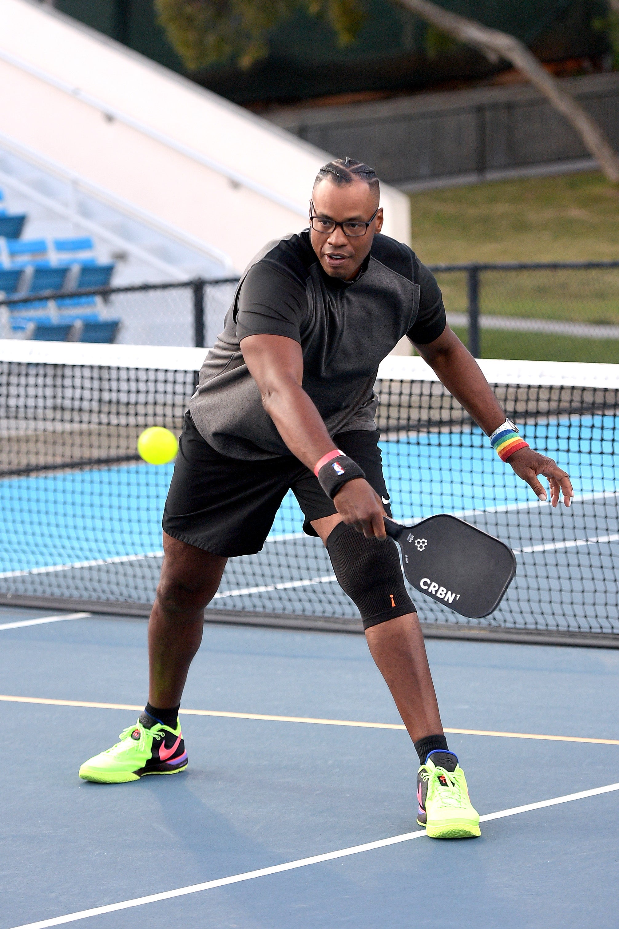 A player in a black shirt and shorts prepares to hit a pickleball with a paddle on a court.