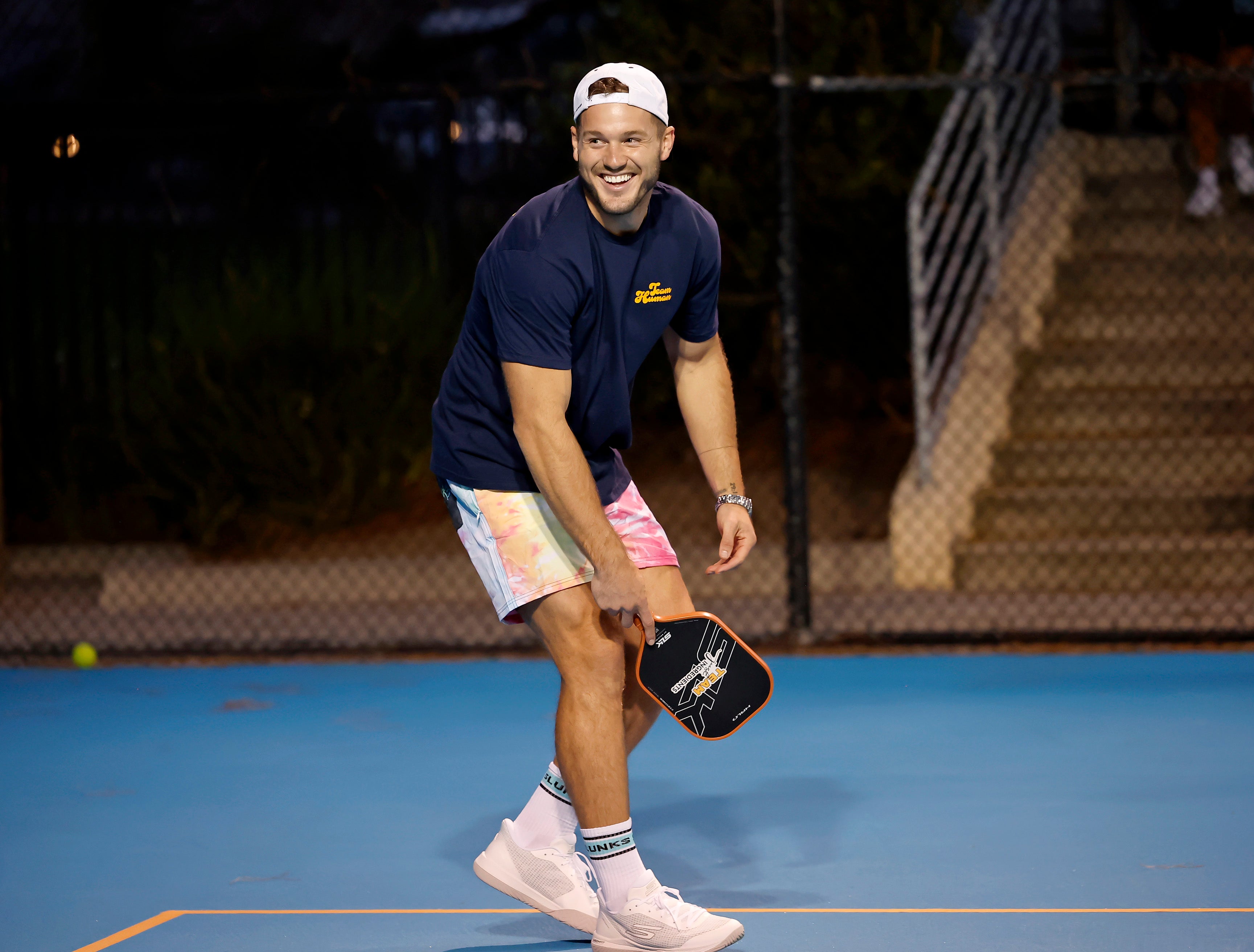 Colton Underwood smiling while holding a pickleball paddle on a court