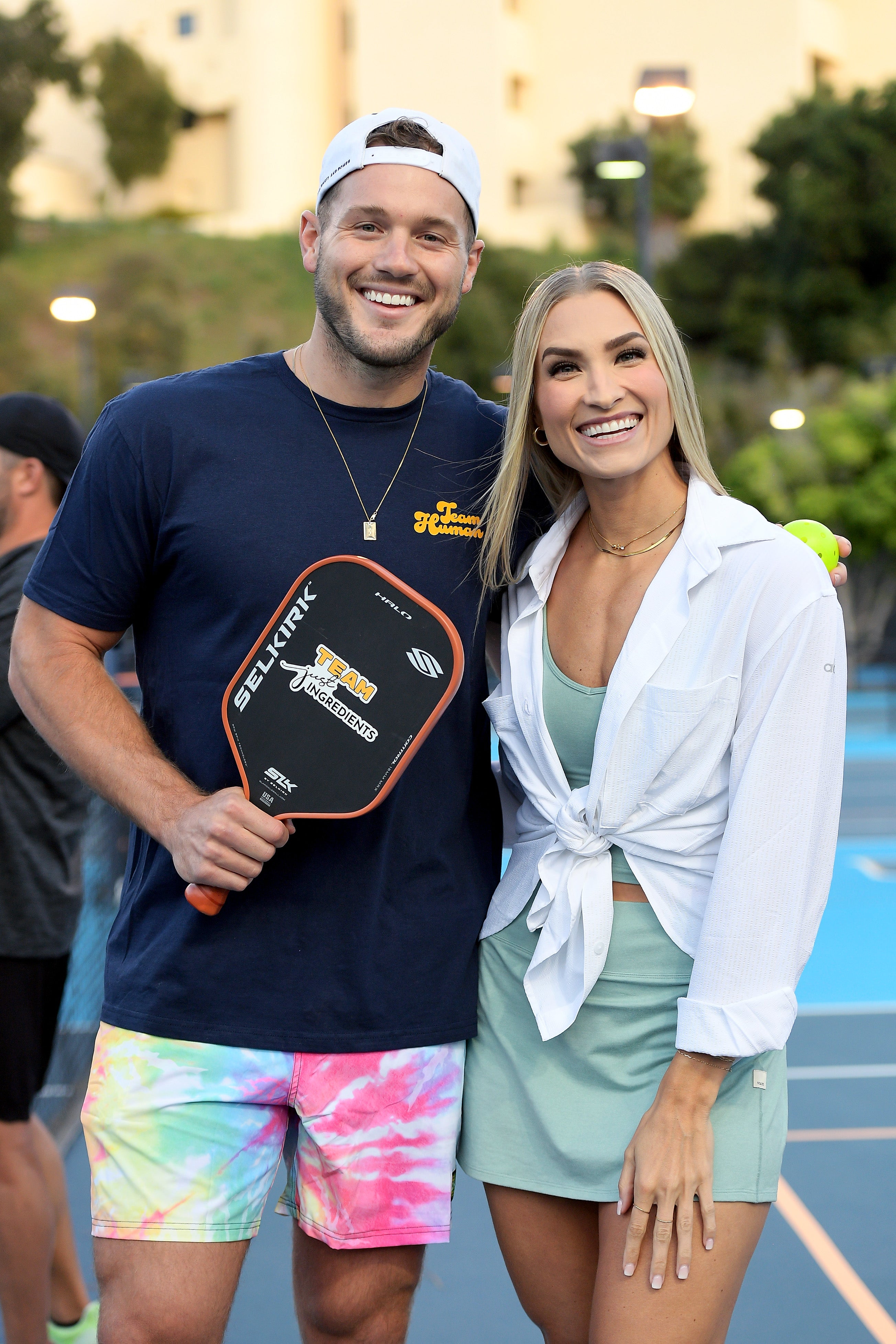 Colton Underwood and a woman smiling, holding a pickleball paddle, at a pickleball event.