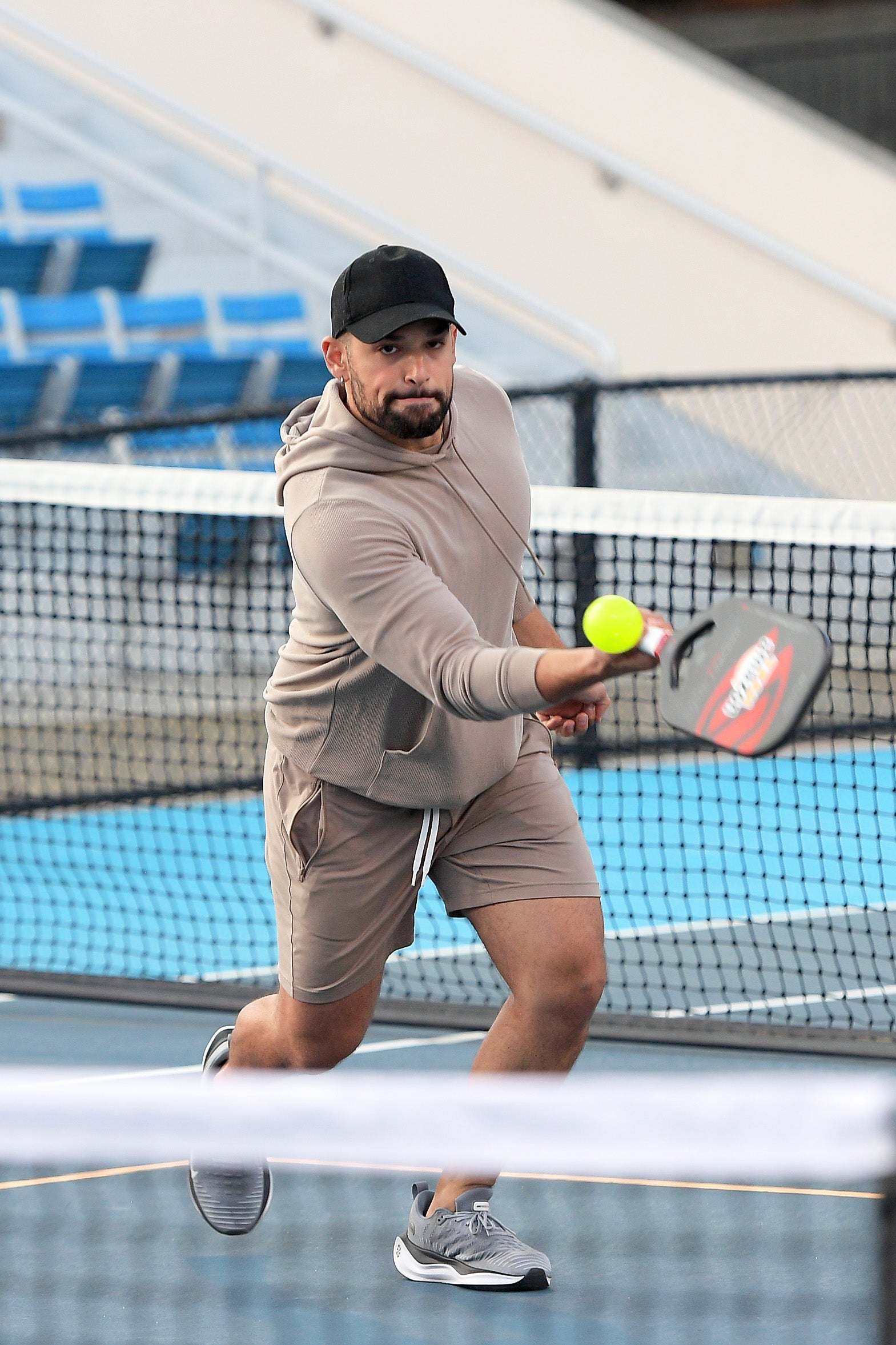 A man in a beige outfit and cap hitting a pickleball during a match.