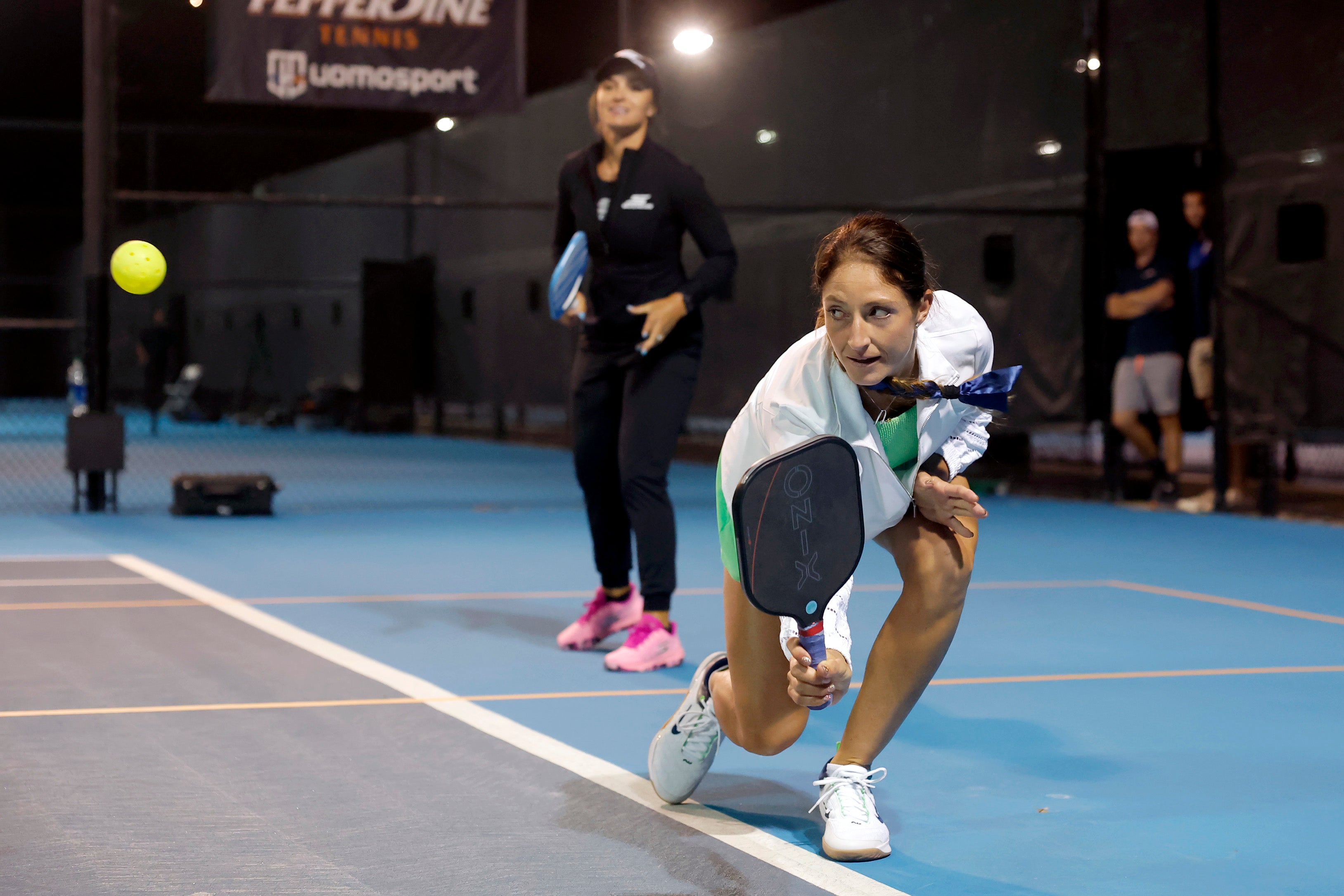 A player in a pickleball match prepares to hit the ball with a paddle, while another player is in the background.