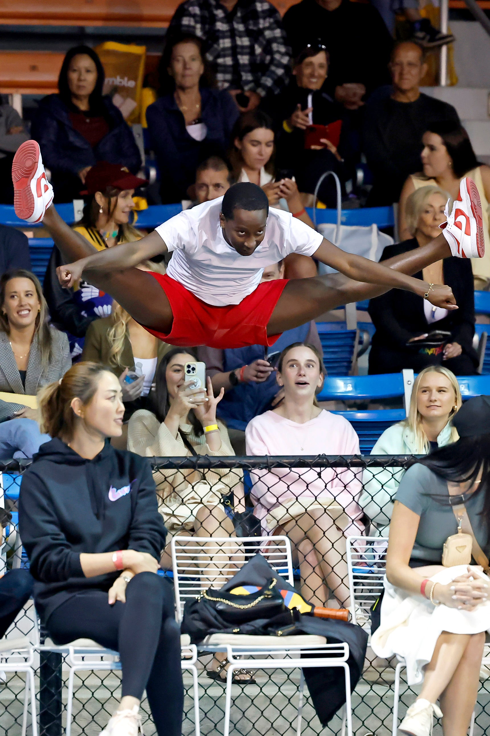 A person performing a high jump during a pickleball event, with spectators in the background.