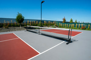 Selkirk Semi-Permanent Pro Pickleball Net set up on a court with red playing surface and green background.