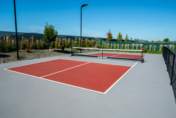 Selkirk Semi-Permanent Pro Pickleball Net set up on a red court with surrounding greenery.