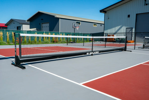 Selkirk Semi-Permanent Pro Pickleball Net set up on a court with a gray surface and red markings.