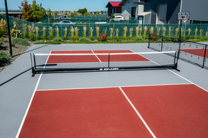 Selkirk Semi-Permanent Pro Pickleball Net set up on a court with red and gray surfaces.