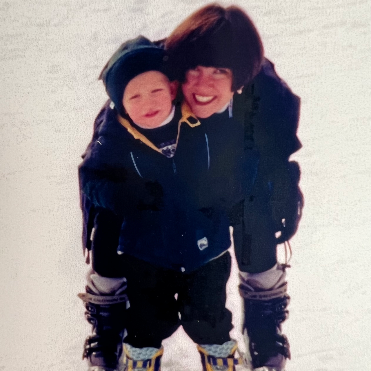 A mother and child smiling together on skis, showcasing their bond and support.
