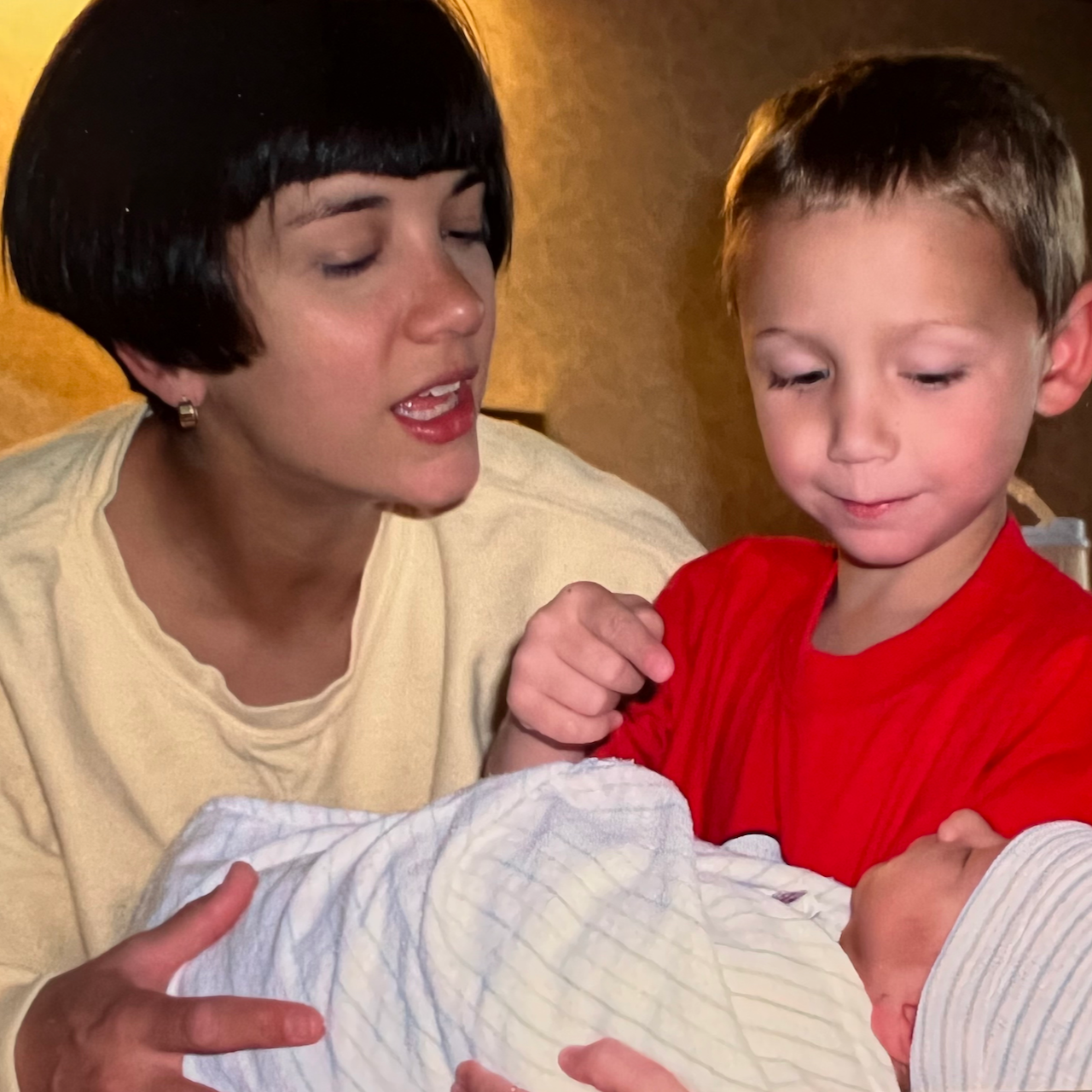 A mother holding a baby while a young boy points at the baby, conveying family support and love.