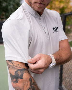 Man adjusting sleeve of Selkirk TruWear Men's Vortex Lifestyle Collared Polo, showing tattoo.