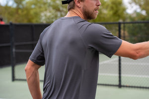 A man wearing a Selkirk TruWear Men's Cardinal Workout Shirt, showing the back view on a tennis court.