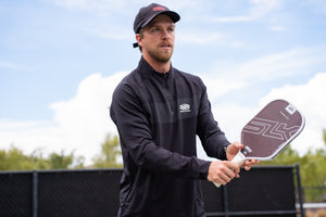 Man wearing Selkirk TruWear Men's Apex 2.0 Quarter Zip Pullover, holding a pickleball paddle on a court.