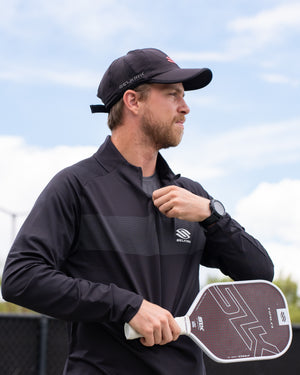 Man wearing Selkirk TruWear Men's Apex 2.0 Quarter Zip Pullover, holding a pickleball paddle.