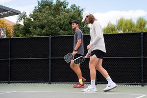 Two men playing pickleball, one wearing a long sleeve shirt.