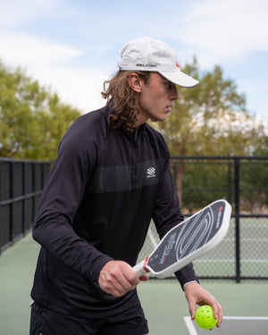Male player wearing Selkirk TruWear Men's Apex 2.0 Quarter Zip Pullover, preparing to hit a pickleball.