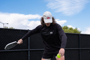 A man playing tennis wearing the Selkirk TruWear Men's Apex 2.0 Quarter Zip Pullover in black.