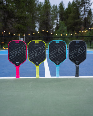 Four SLK HALO Control paddles in pink, yellow, blue, and black on a court
