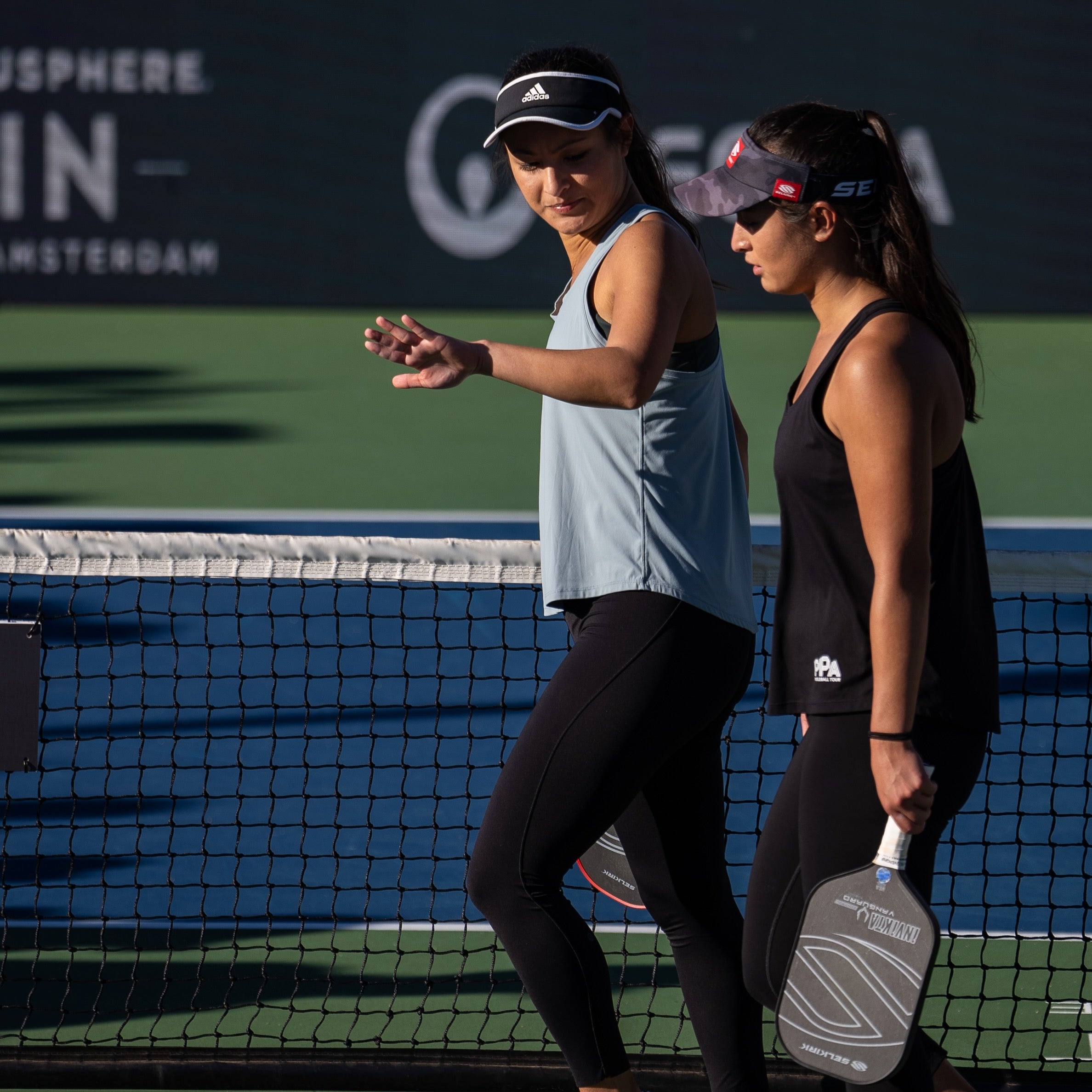 Pickleball pros Jade and Jackie Kawamoto walking on a pickleball court, discussing strategy.