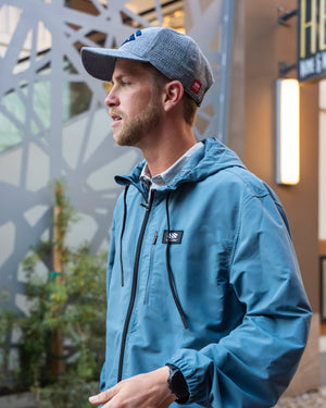 A man wearing a blue Men’s Bunker Lightweight Hooded Windbreaker outdoors.