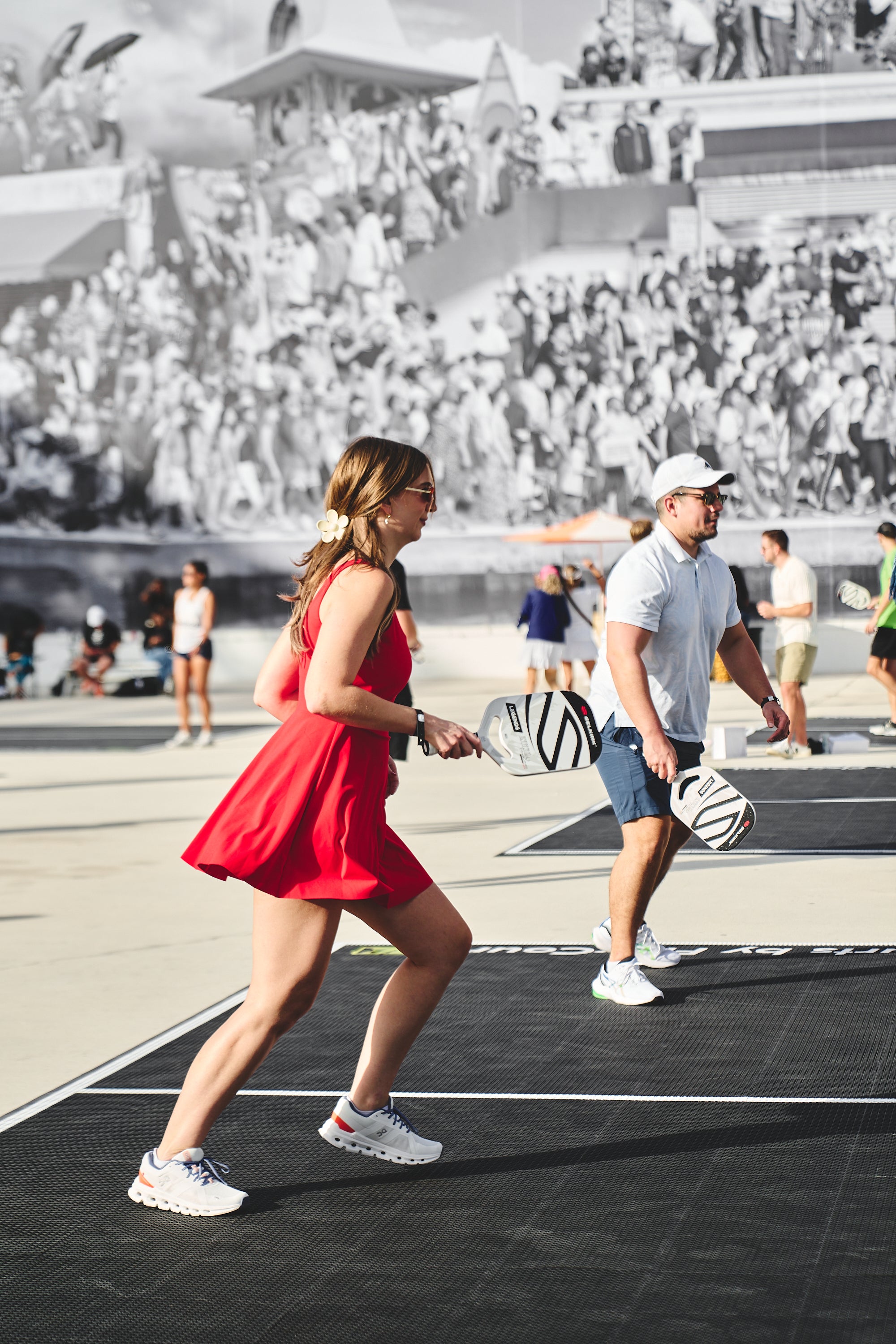 Two players participating in a pickleball game, one in a red dress and the other in a white shirt, with a crowd in the background.